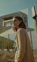 a woman in a trench coat is standing outside a house