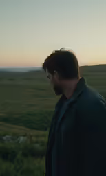 the man stands looking down a grassy plain