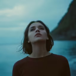 a woman looking upward while standing next to a body of water