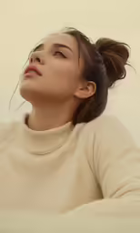 a woman wearing a long white sweater looks up