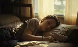 a woman laying in bed with her hands on the pillows