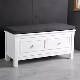 a white bench sitting against a gray wall