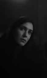 a woman wearing a black coat is staring into the distance