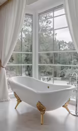 an elegant, white bathtub and gold trim by a window