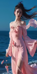 a woman in a pink dress standing on the beach with her long hair blowing in the wind
