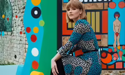 a woman sitting on the ground next to some colorful paintings