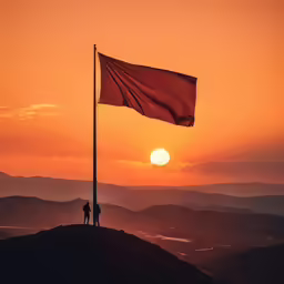 two people are on the top of a mountain looking at a flag