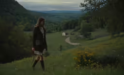 a woman standing in a green field, staring over the countryside