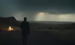 man in a dark coat standing under stormy sky overlooking countryside