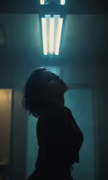 a woman in an elevator hall looks up at a light that is shining down
