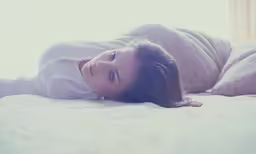 a woman lays on a mattress in the sunlight