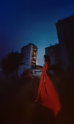 a woman in a red dress is walking in a field near a tall building