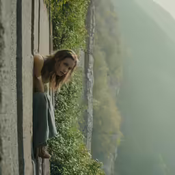 a girl standing on an outside wall holding her hands out