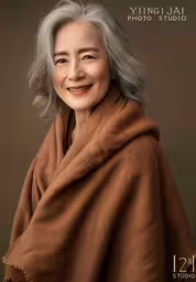 the older woman has gray hair and smiles for the camera,a woman wearing a tan shawl posing for a portrait