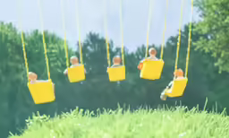 two people sitting on yellow swings in the grass