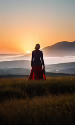 a woman in a dress standing at sunset on the mountain top
