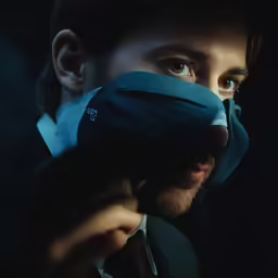a man holding a glove over his eyes in the dark