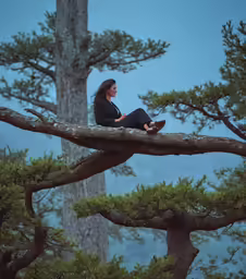 the woman is sitting on a tree branch while looking at her phone