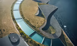 an aerial view of the exterior of the curved concrete house with water running from it