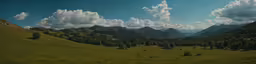 a green valley and mountains under some clouds