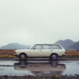 an older style station wagon with no door stands in a body of water, in front of mountains