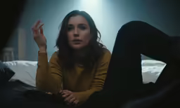 a woman is holding her hand up while sitting on a bed