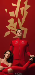 a man in red suit and woman wearing red in front of a gold leaf