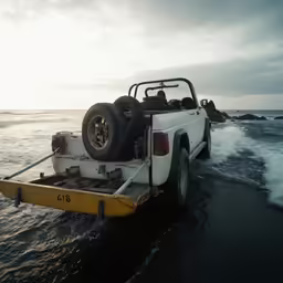 a truck with a flat bed is riding through the ocean