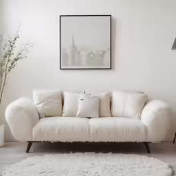 a white couch with pillows in front of a picture on the wall