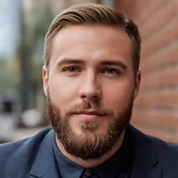 a bearded young man wearing a suit and tie looking at the camera