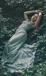 a young woman laying in the leaves of a green forest