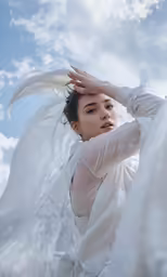 a beautiful woman in white is holding her head with wings