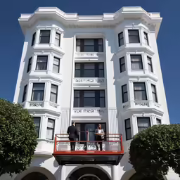 two men in suits and ties stand on a balcony overlooking a building with trees