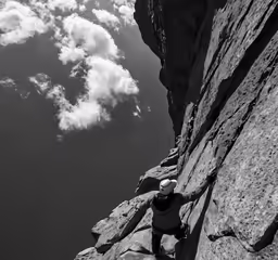 a climber rapping up a steep rock face in front of a cloudy sky