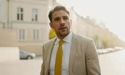 a man in a tan jacket and yellow tie looks confused