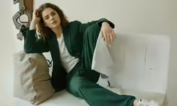woman sitting on a couch in a green suit and sneakers