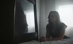 a woman sitting on a bed while looking in the mirror