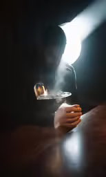 man in black jacket lighting a candle over the top of a plate