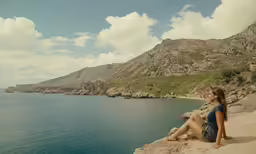 a woman sitting on the rocks near the water