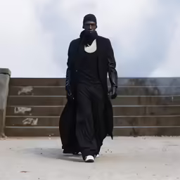 a man walking down a concrete walkway in a black suit