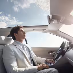 a man in white suit sits in front of his car and works on his computer