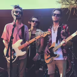 three guys in glasses standing near each other,two men holding guitars while standing in front of microphones
