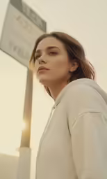 a woman looking away while standing next to a street sign