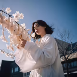 a woman standing next to a tree holding white flowers