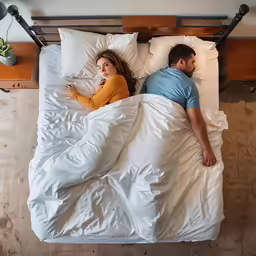 a man and woman laying in bed with their sheets down