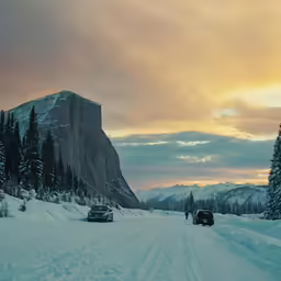 vehicles driving on snow covered road in front of mountain