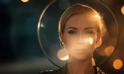 a woman in black jacket standing under a light - like halo