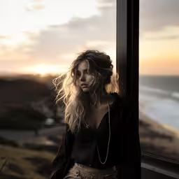 a woman in black blouse and tan pants leaning against the window,the woman in the photo has ear phones to her ear