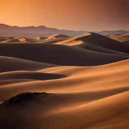 sand dunes in the distance at sunset with mountains in the background