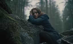 a person with their hand on the side of their face, sitting on a rock